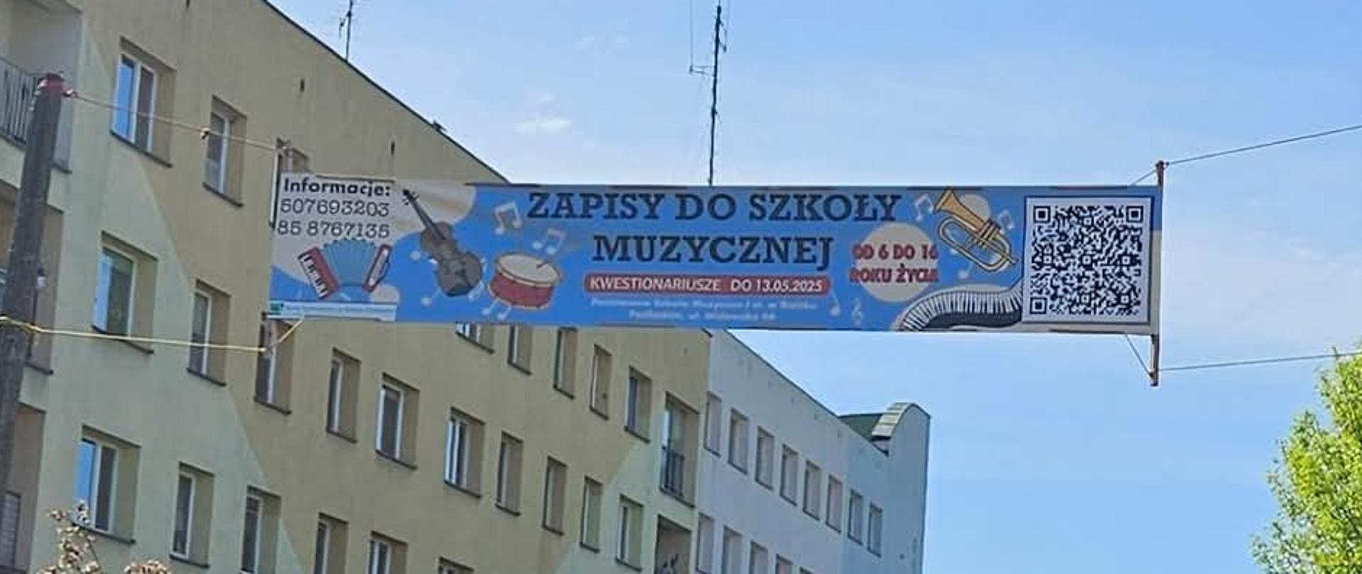 Ulica miasta, a nad nią rozwieszony baner informujący o zapisach do szkoły muzycznej. Dominuje kolor błękitny, są instrumenty muzyczne, kod QR i inne potrzebne informacje.