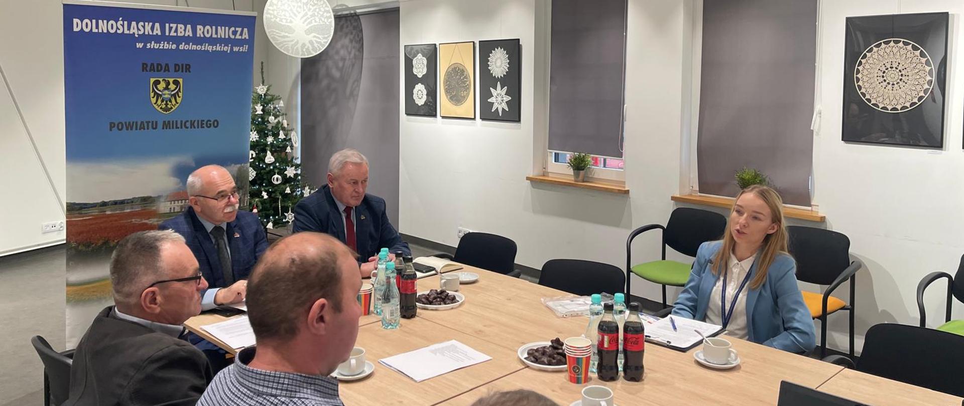Uczestnicy Posiedzenia Rady Powiatowej DIR powiatu milickiego siedzący w sali konferencyjnej przy prostokątnym stole. Uczestnicy patrzą w stronę przemawiającej Inspektor z Oddziału W Miliczu.