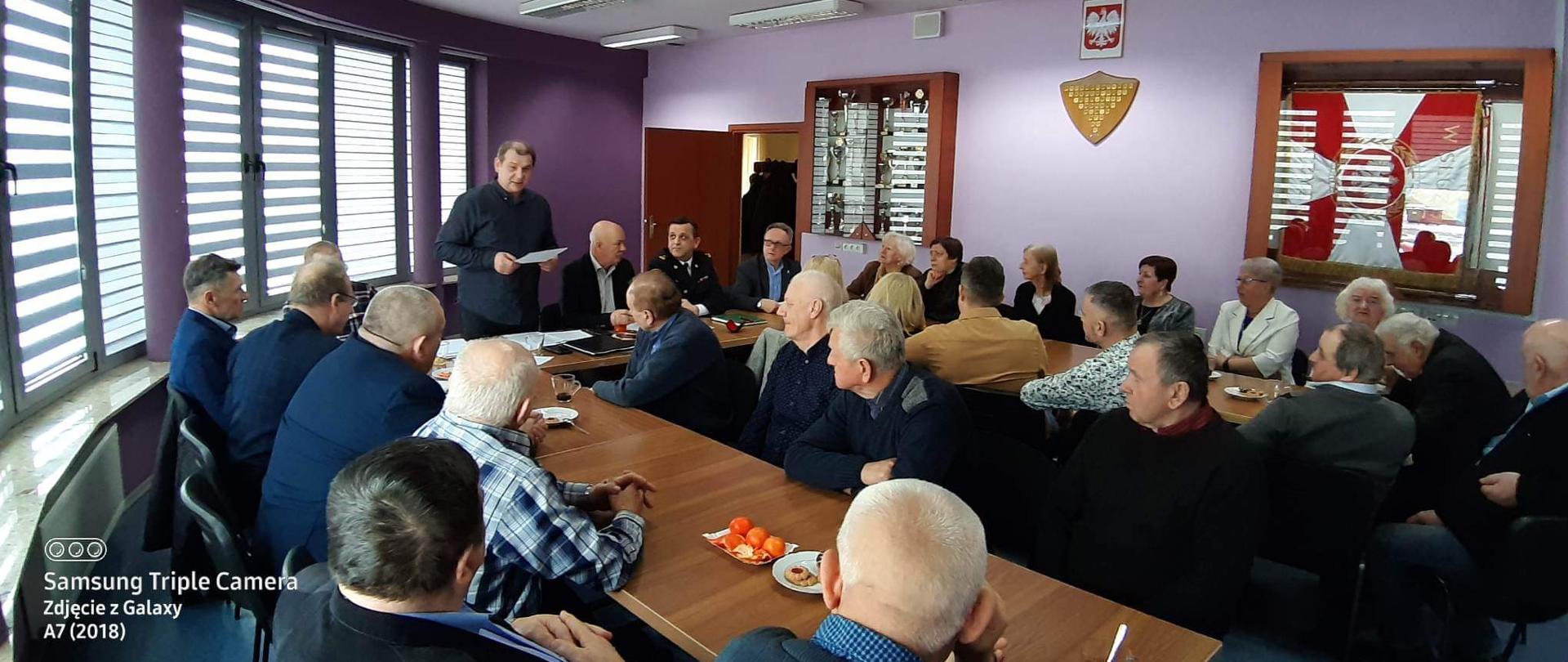 Sala Narad Komendy Powiatowej Państwowej Straży Pożarnej we Włoszczowie, członkowie koła emerytów i rencistów siedzą przy stołach ustawionych w podkowę, przy stole prezydialnym ustępujący zarząd wraz z przedstawicielem zarządu oddziału wojewódzkiego oraz komendantem powiatowym PSP we Włoszczowie, odczytywane jest sprawozdanie z działalności koła za okres sprawozdawczy