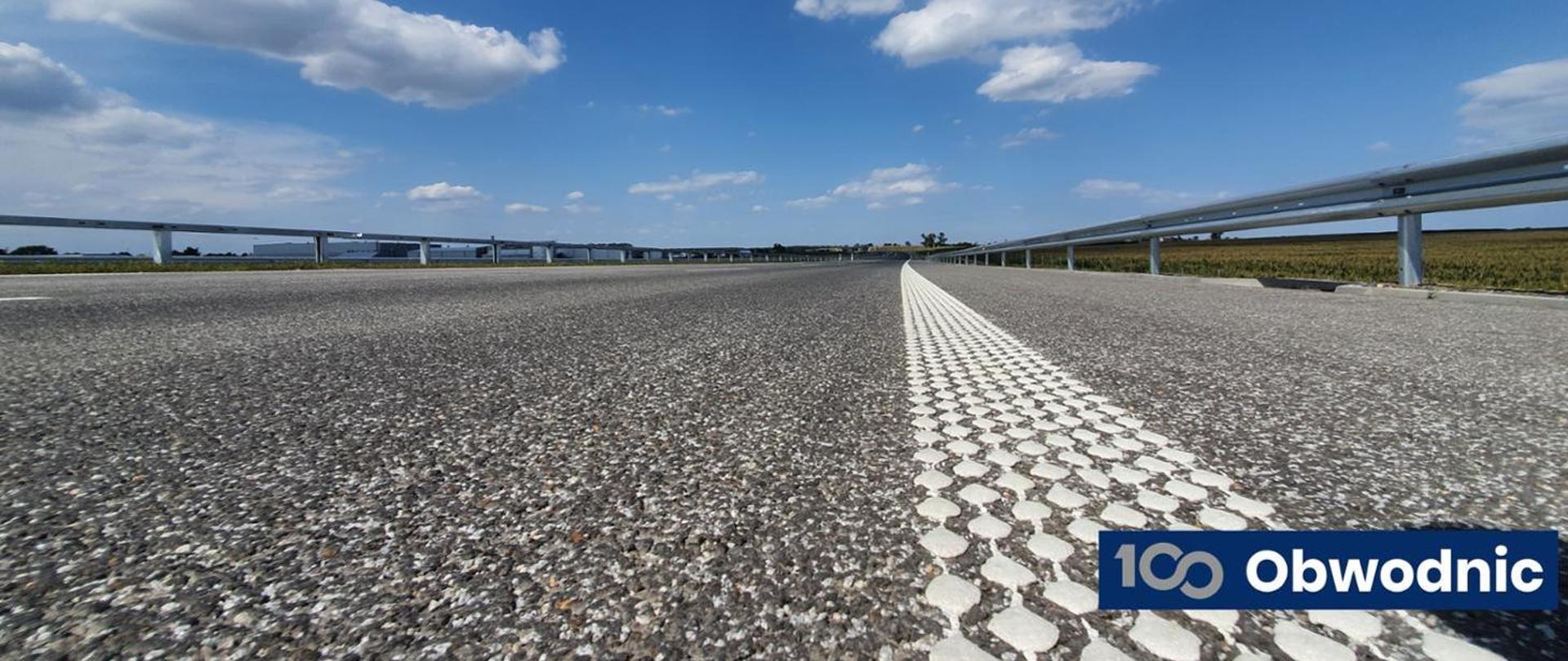 Na zdjęciu widoczna jest jezdnia oraz logo programu budowy 100 obwodnic.