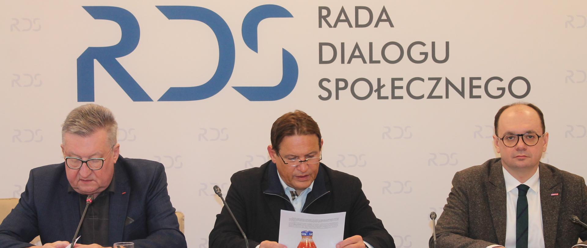 Na zdjęciu widnieje stół prezydialny za którym siedzą: Pan Wojciech Nagel, Przewodniczący Zespołu ds. ubezpieczeń społecznych; Pan Jacek Męcina, Przewodniczący Zespołu ds. prawa pracy oraz Pan Sebastian Gajewski, Podsekretarz Stanu w Ministerstwie Rodziny, Pracy i Polityki Społecznej. W tle widnieje baner z napisem Rada Dialogu Społecznego