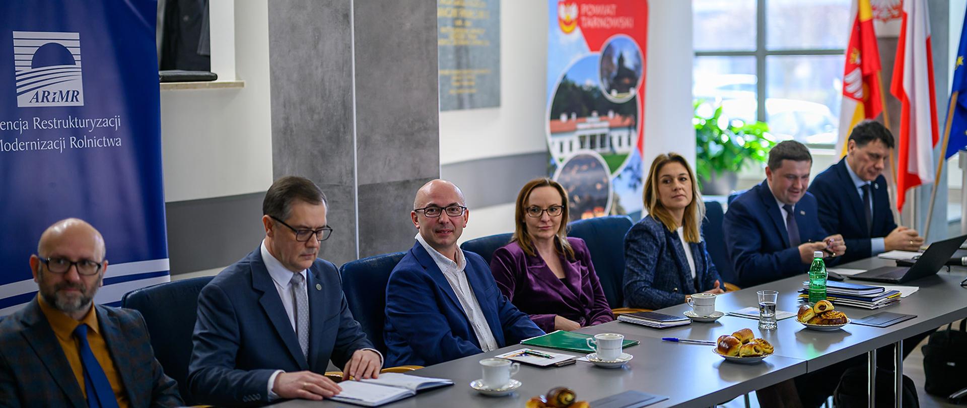 Uczestnicy spotkania (kobiety i mężczyźni) siedzący przy stole konferencyjnym