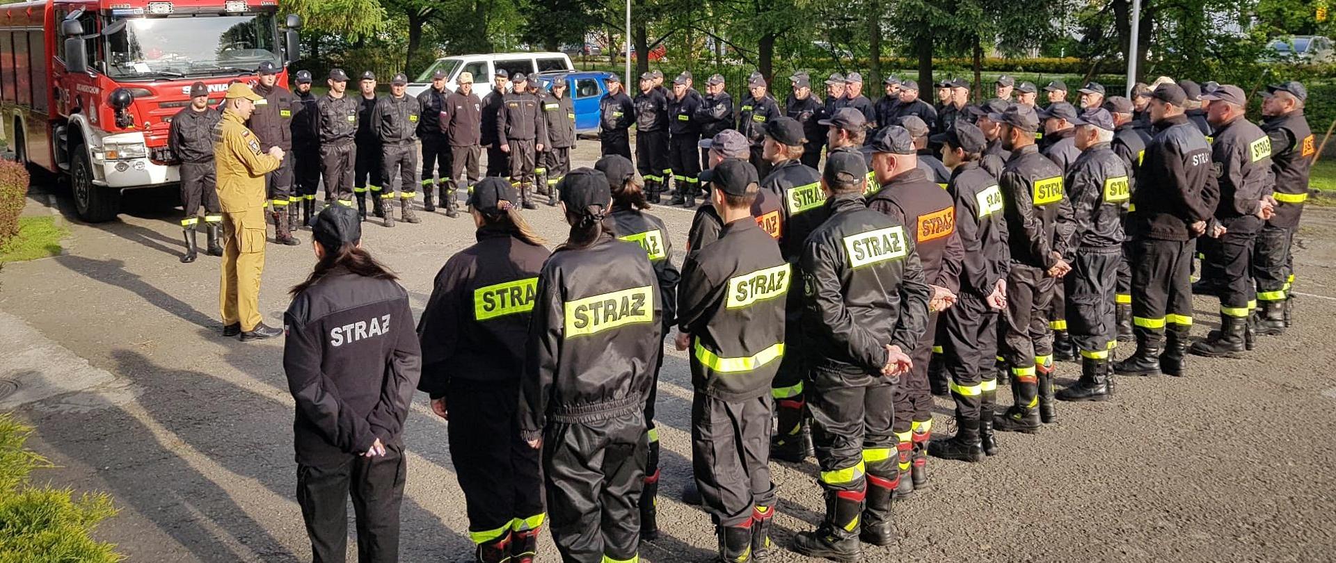 Widok z tyłu. Uczestnicy szkolenia na zbiórce z instruktorem z PSP. 