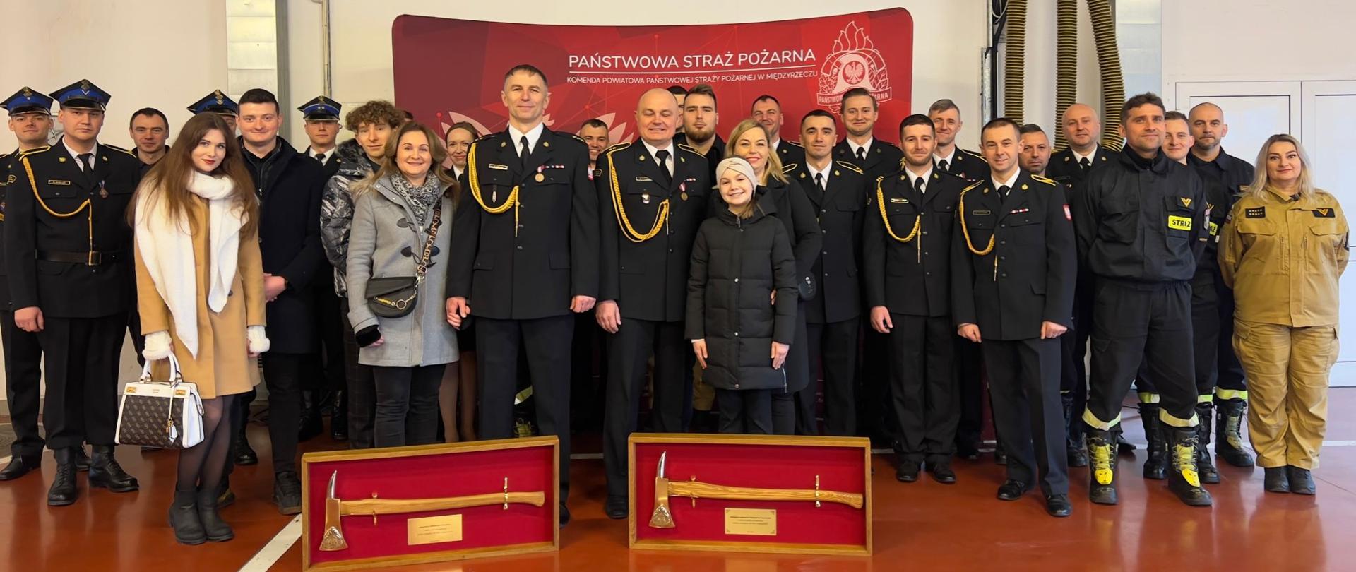 Zdjęcie przedstawia biorących udział w uroczystości funkcjonariuszy KP PSP Międzyrzecz oraz rodziny odchodzących na emeryturę strażaków.
