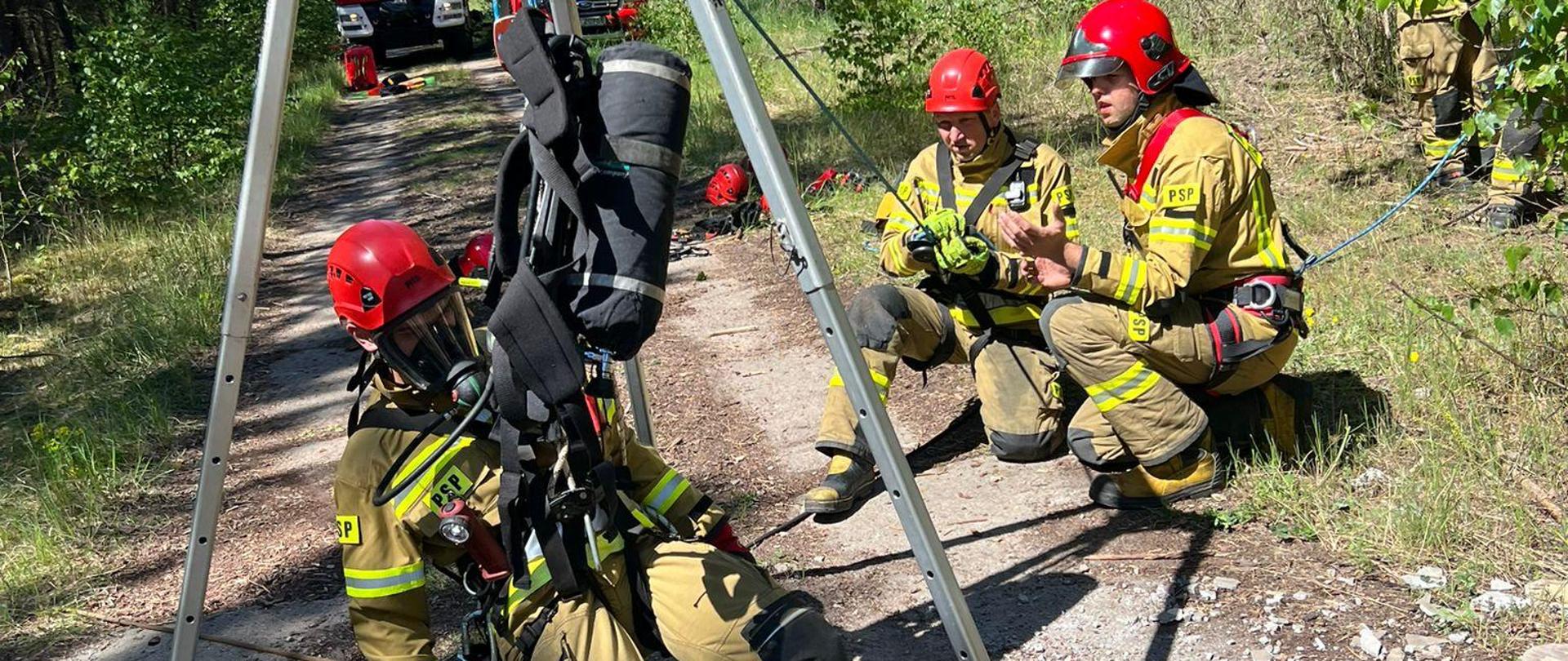 Ratownik podwieszony na trójnogu ewakuacyjnym przed opuszczeniem do studzienki.
