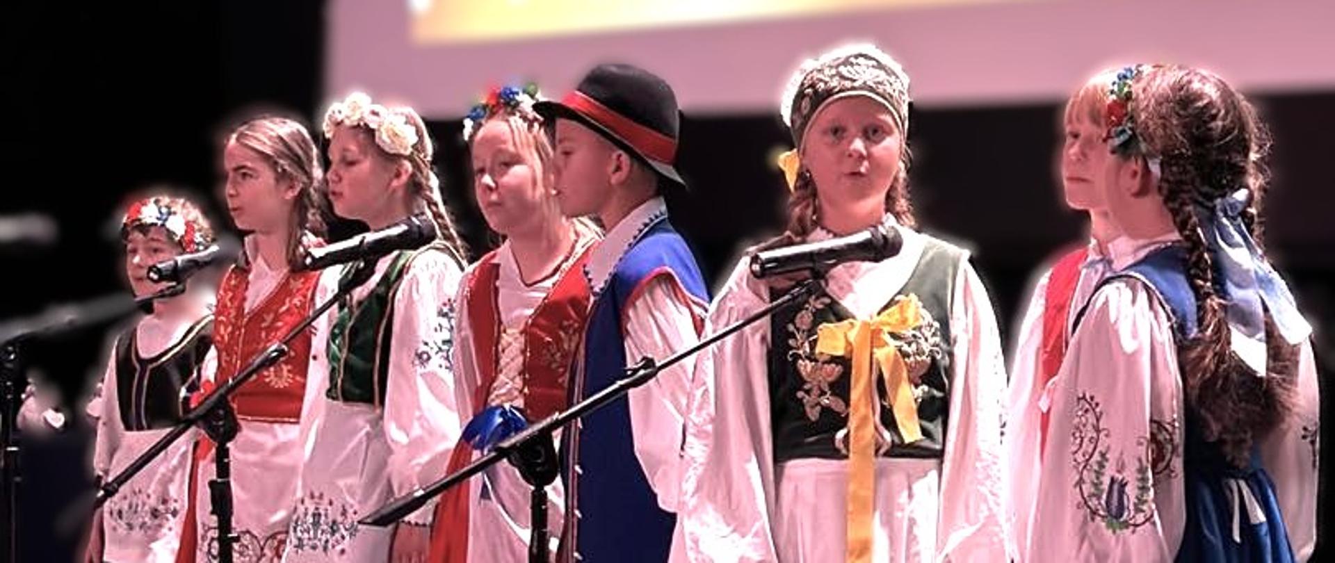 dzieci w strojach ludowych kaszubskich stoją na scenie i śpiewają