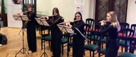 Zdjęcie przedstawia kwartet fletowy, złożony z czterech uczennic POSM II stopnia podczas występu na scenie w holu Pałacu Radolińskich.