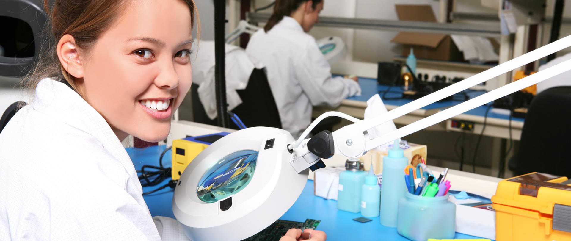 Uśmiechnięta dziewczyna siedzi przy stole laboratoryjnym.