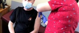 Strażak siedzi pani pielęgniarka dokonuje szczepienia