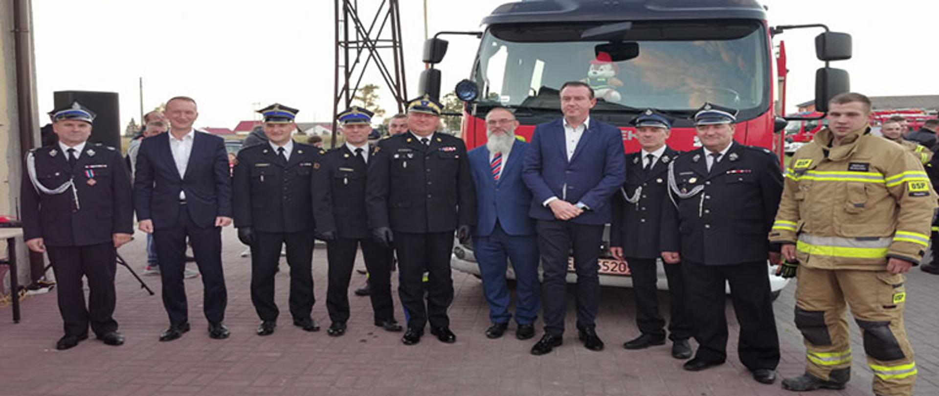 goście w ilości dziesięciu osób stoją przed samochodem strażackim pozując do pamiątkowego zdjęcia
