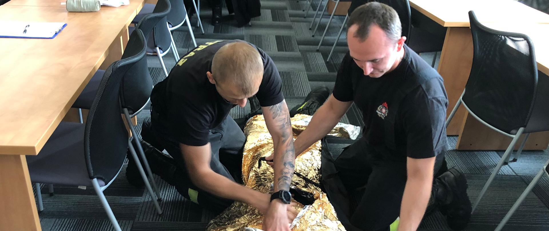 Na trzecim zdjęciu strażacy-ratownicy taktyczni przygotowują poszkodowanego do ewakuacji z pola walki.