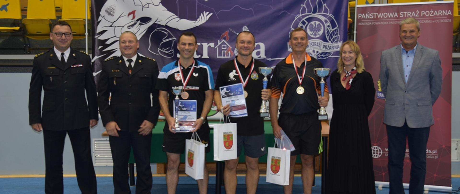 Na tle baneru mistrzostw Województwa Starzaków w tenisie stołowym stoją zwycięzcy turnieju, Komendanci PSP oraz sponsorzy.