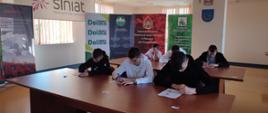 Uczestnicy turnieju piszący test wiedzy, w tle banery sponsorów turnieju..