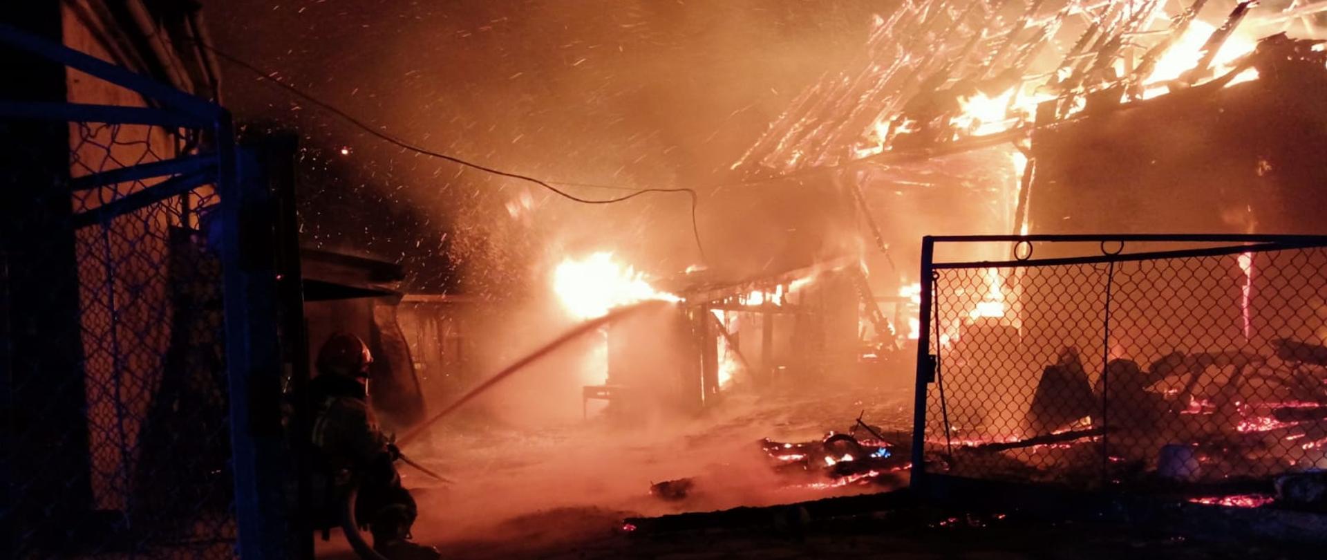 Pożar całkowity budynku gospodarczego. Z lewej strony strażak podaje prąd wody na źródło ognia.