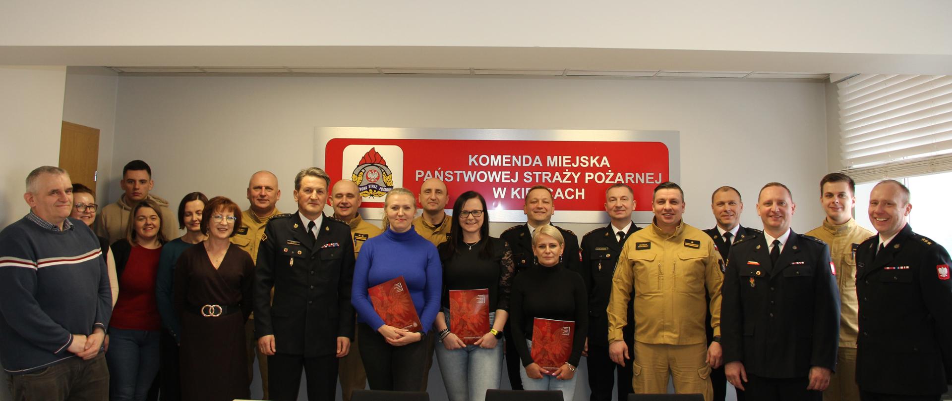 Fotografia przedstawia funkcjonariuszy i pracowników cywilnych ustawionych do pamiątkowego zdjęcia. W pierwszym rzędzie stoi kadra kierownicza tutejszej komendy oraz pracownice Służby Cywilnej.