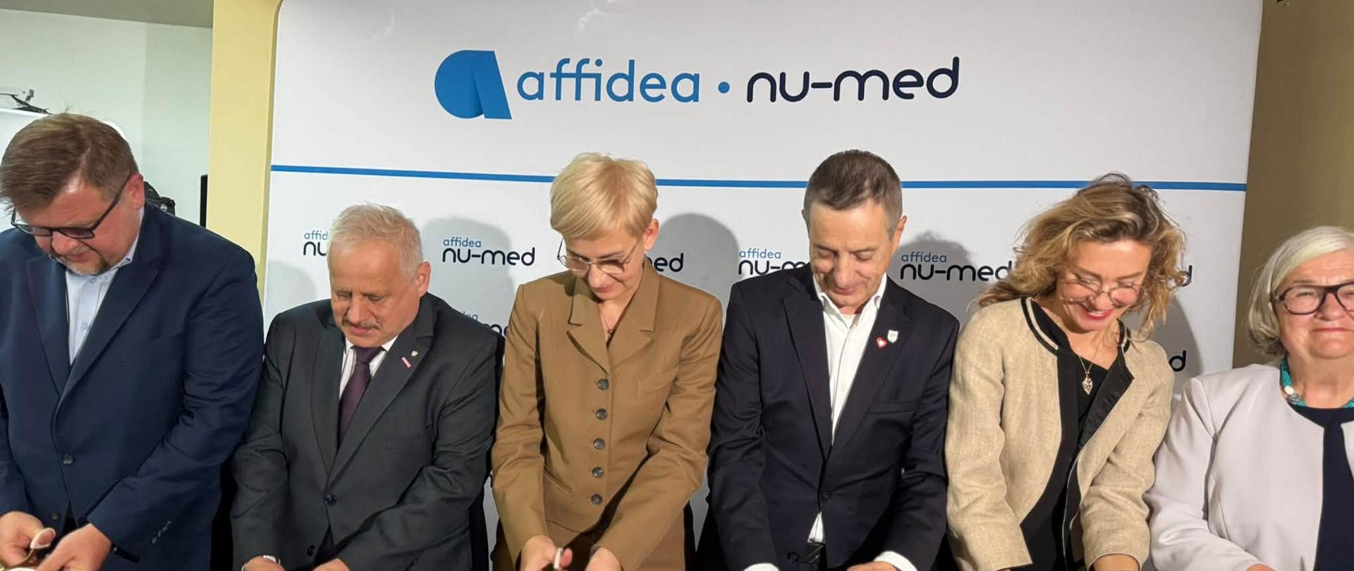 Grupa kilkunastu osób stoi przed sala i przecina czerwoną wstęgę 