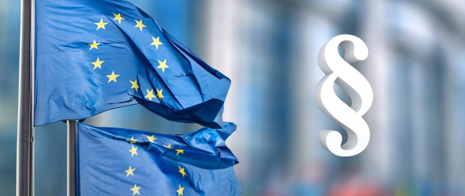 Flagi Unii Europejskiej powiewające na tle nowoczesnego budynku, obok biały symbol paragrafu oznaczający regulacje prawne UE.