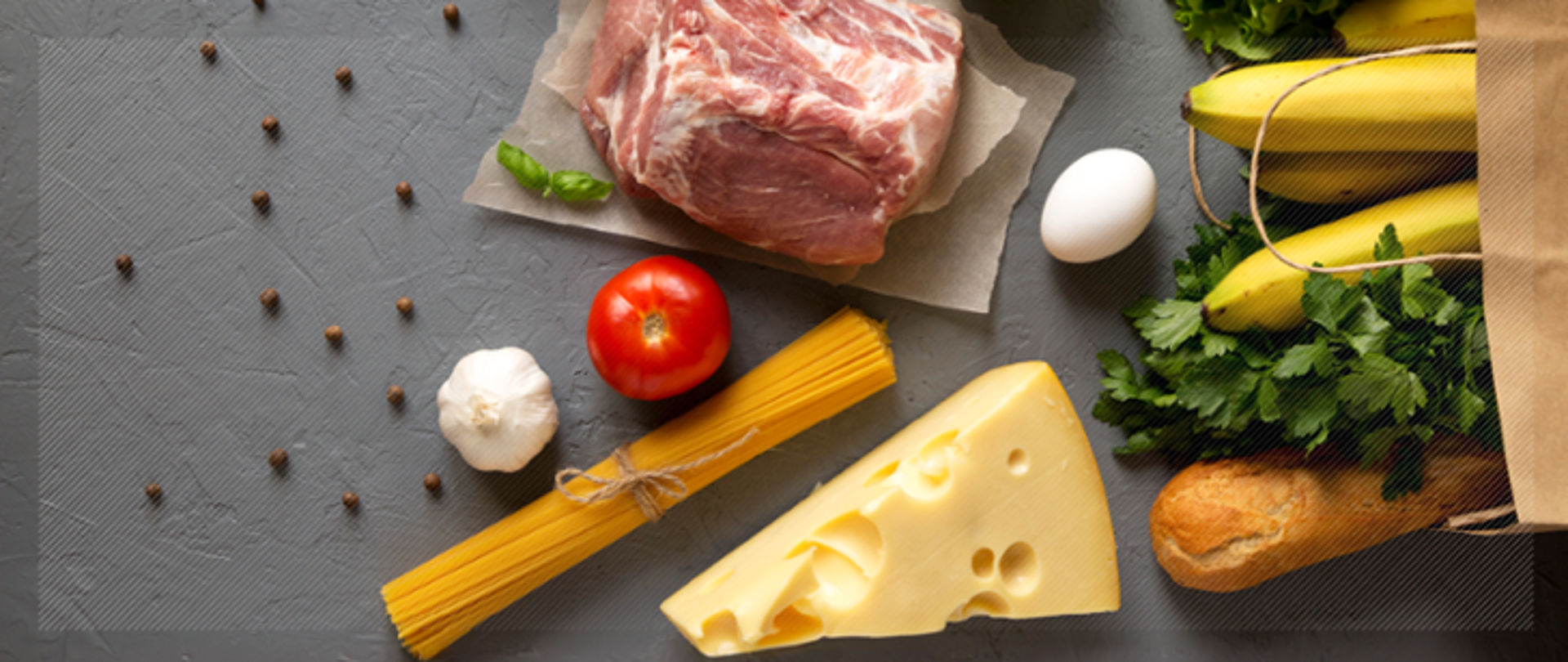 Zdjęcie przedstawia żywność: surowe mięso, ser żółty, makaron, jajko, czosnek, pomidor, pietruszkę, bagietkę banany. 