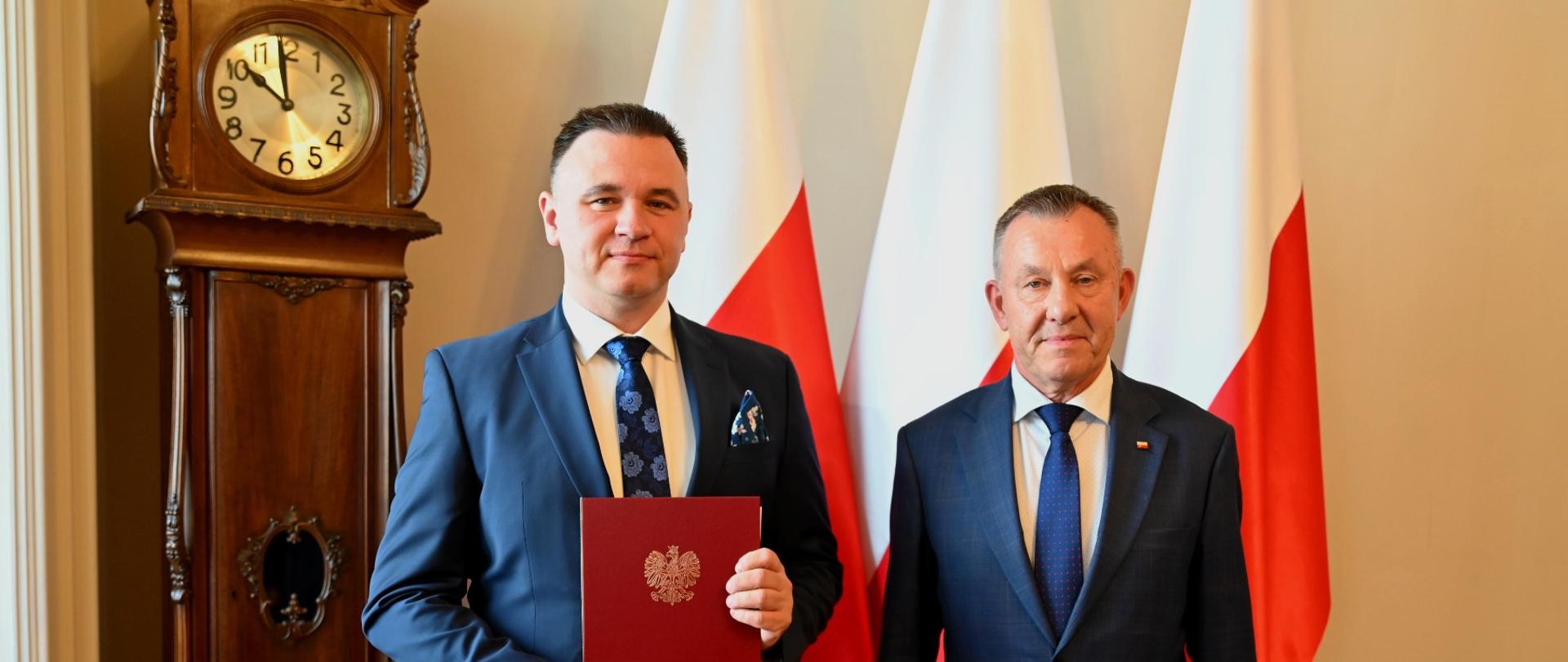 wojewoda łódzki Karol Młynarczyk z konsultantem do spraw alergologii Marcinem Kurowskim na tle biało czerwonych flag