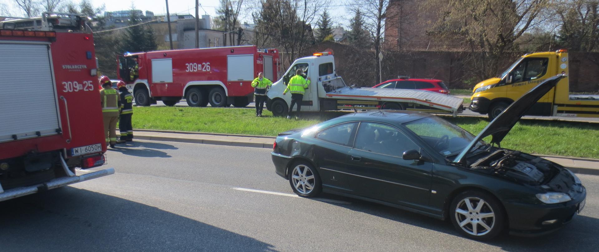Na zdjęciu widoczne są dwa pojazdy pożarnicze, uszkodzony samochód osobowy oraz w dalszym planie dwie lawety pomocy drogowej