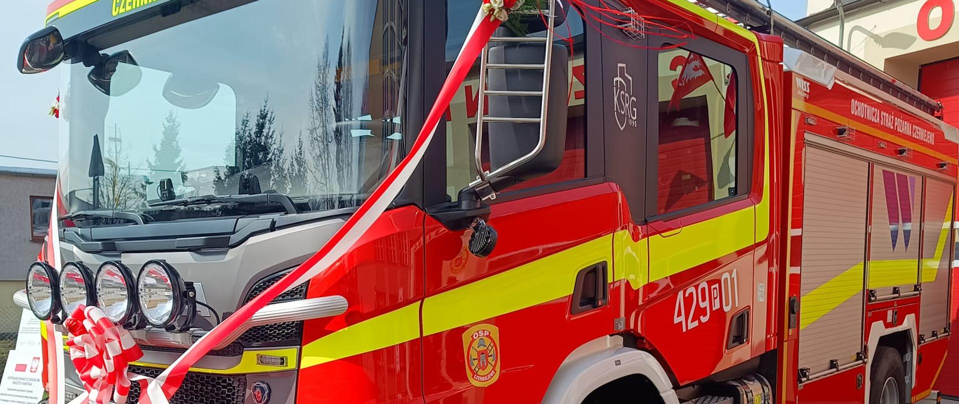 Na zdjęciu widać nowy samochód gaśniczy stojący przed remizą strażacką