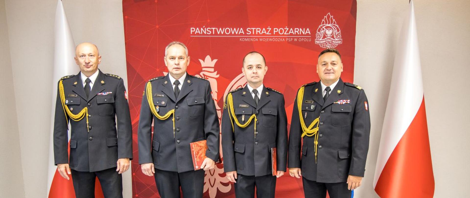 Wspólne zdjęcie nadbryg. Krzysztof Kędryk Opolski Komendant Wojewódzki PSP, st. bryg. Dariusz Gieroń Zastępca Opolskiego Komendanta Wojewódzkiego PSP, st. kpt. Roman Wyszka oraz st. kpt. Marcin Mazur.
Strażacy na tle Flag RP oraz planszy czerwonej z białym napisem Państwowa Straż Pożarna Komenda Wojewódzka PSP w Opolu i Godłem RP.
Strażacy w umundurowaniu galowym.