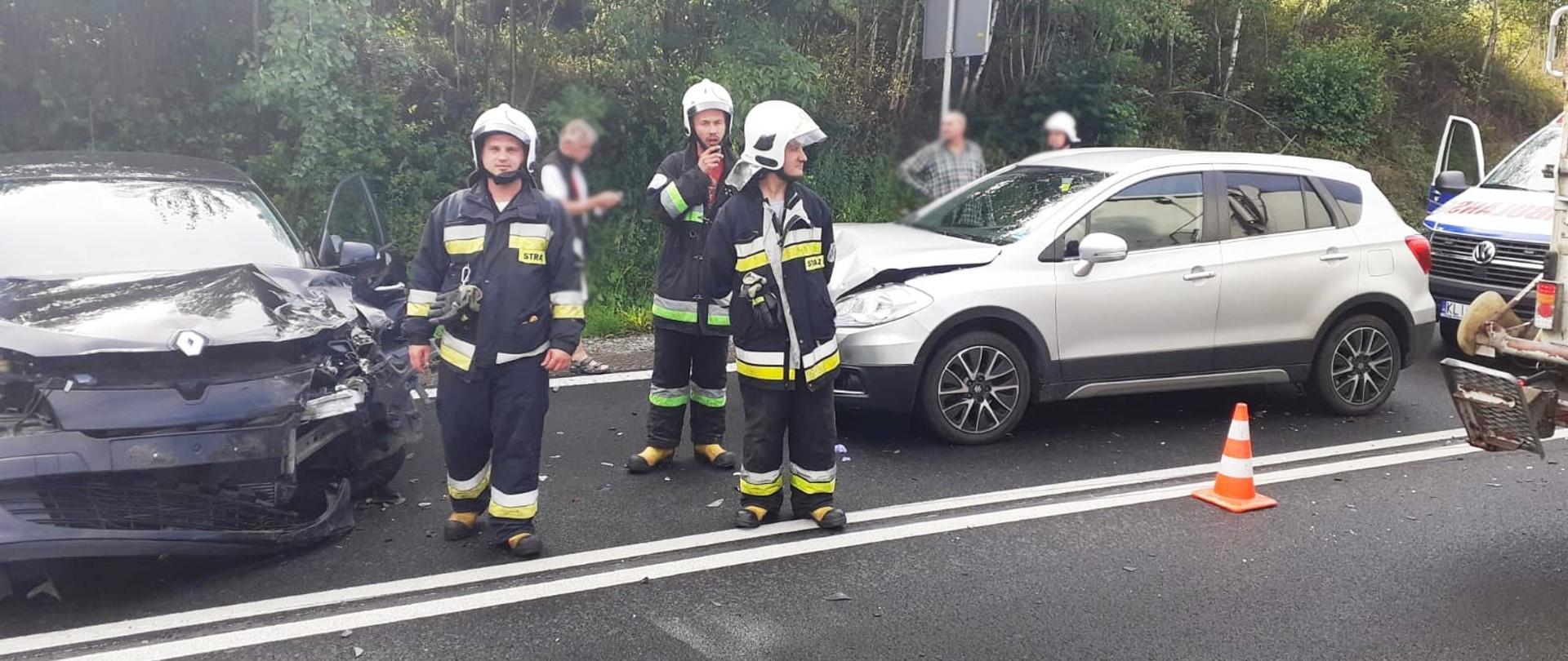 Samochody uczestniczące w zdarzeniu oraz strażacy na drodze.