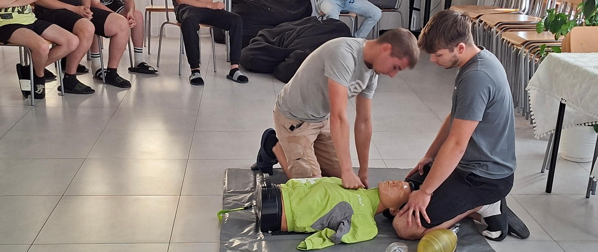 Zdjęcie 2 – Wychowankowie internatu - Filip Grządka i Kacper Drozda prezentują udzielanie pierwszej pomocy, oceniają stan poszkodowanego.