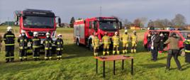 Zdjęcie przedstawia strażaków OSP stojących przed pojazdami podczas uroczystości.
