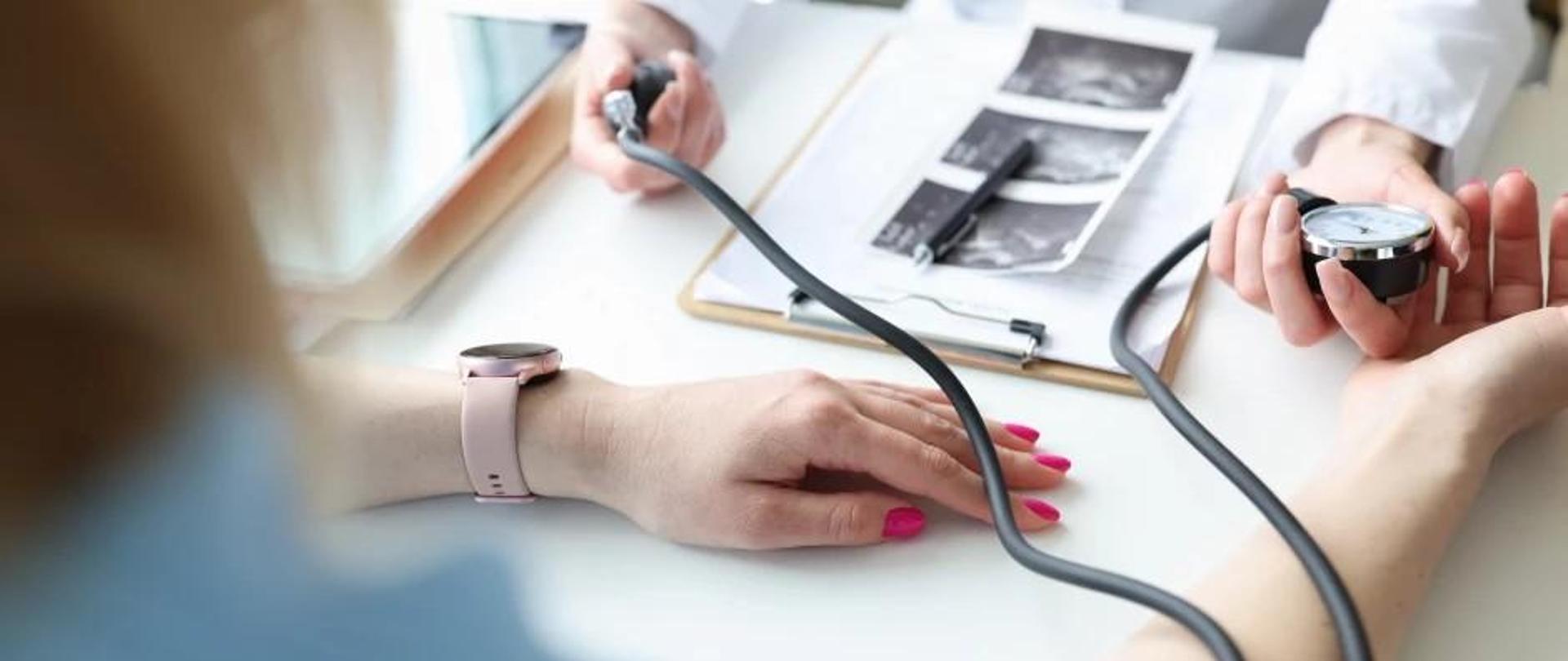 Zdjęcie przedstawiające fragment ludzkich rąk, osób mierzących ciśnienie tętnicze.
