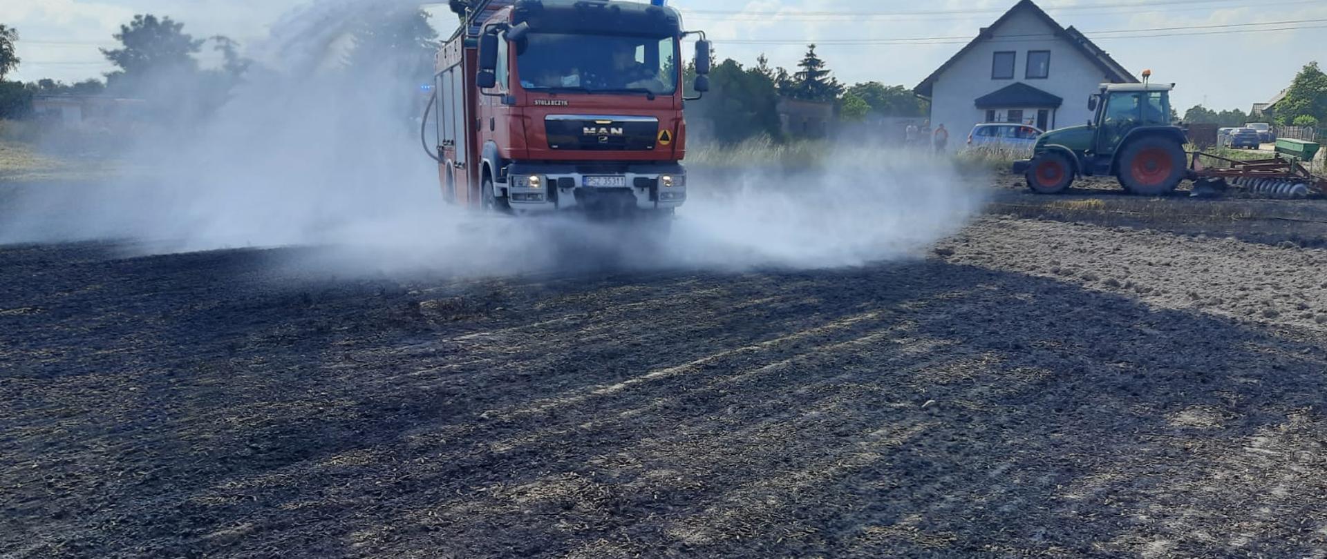 Widać samochód strażacki i ciągnik rolniczy, strażacy gaszą pożar