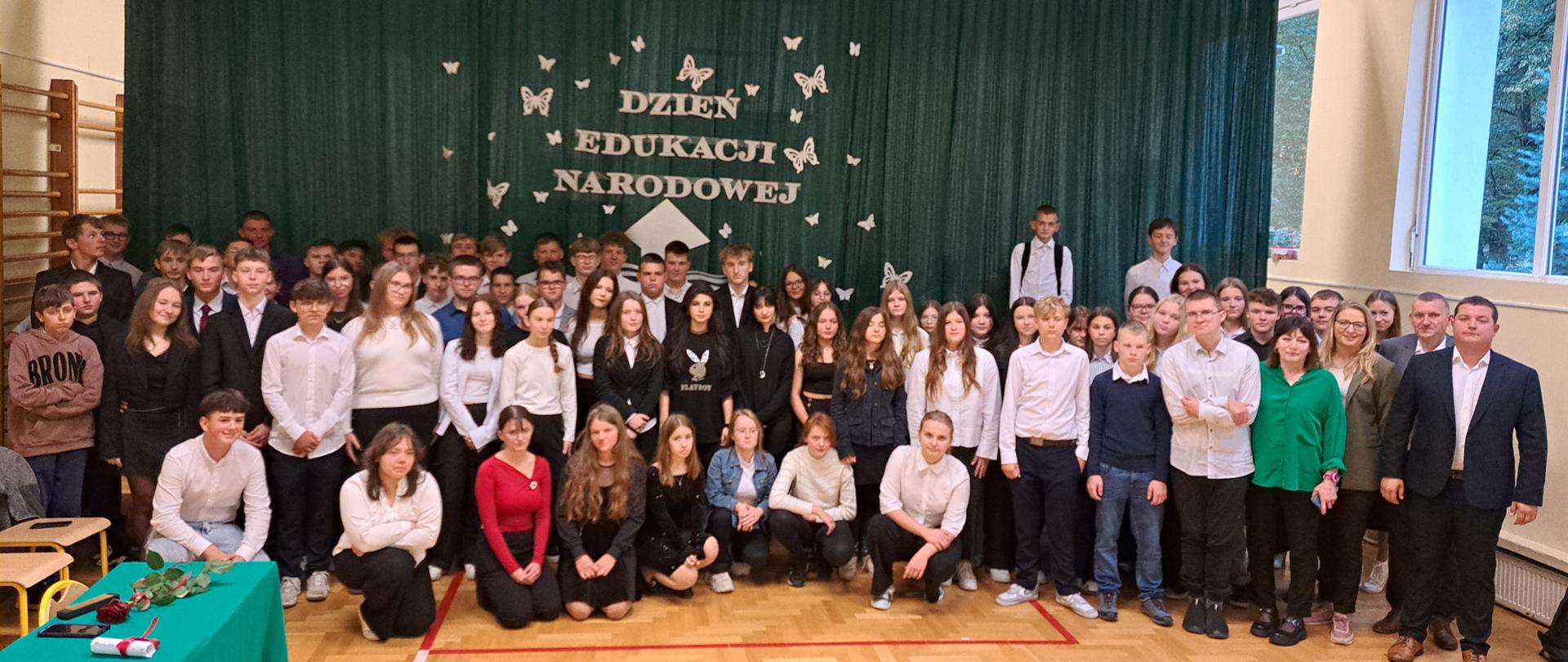 Uczniowie klas pierwszych wraz z wychowawcami na tle okolicznościowej dekoracji