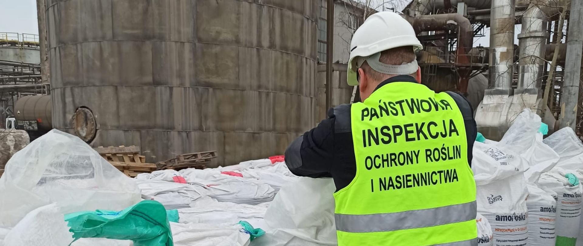 Mężczyzna w odblaskowej kamizelce stoi przy dużych białych workach
