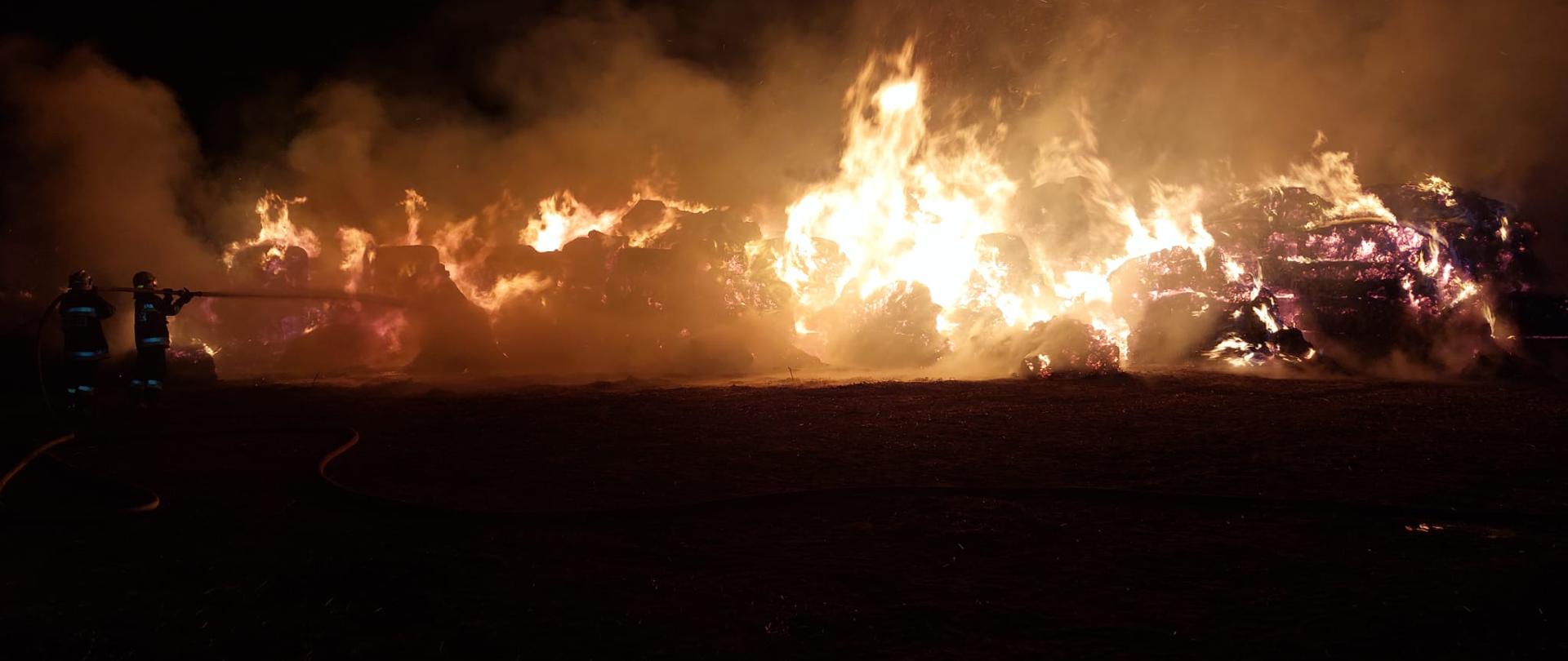 Strażacy podają prądy wody na palącą się stertę słomy