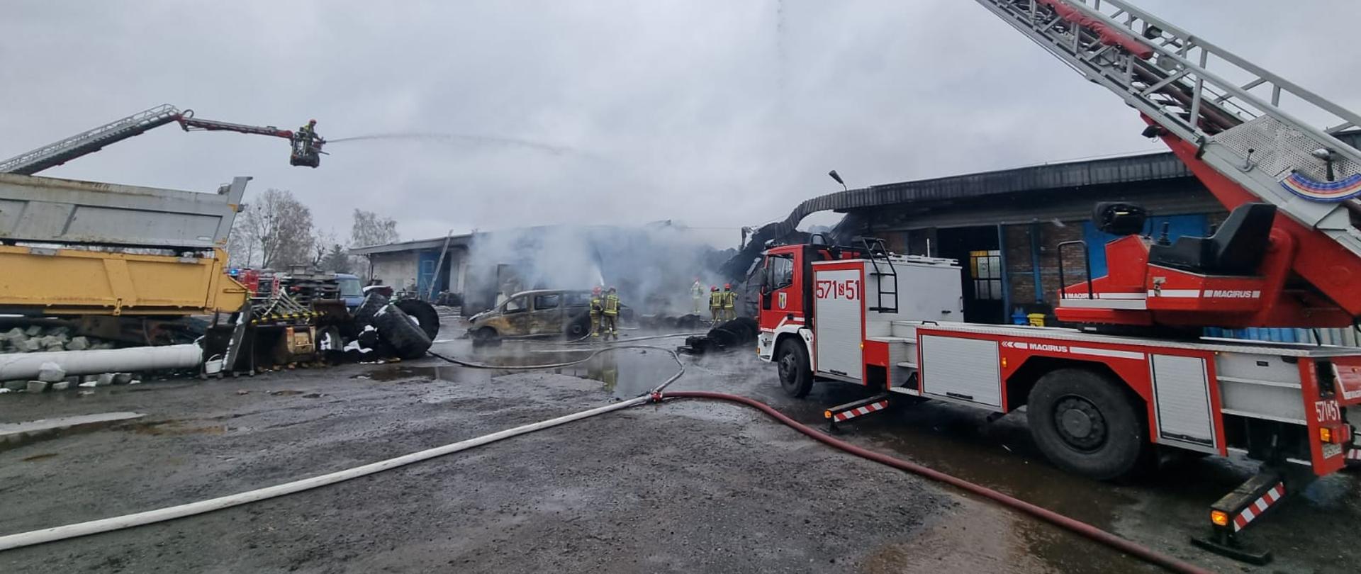 Zdjęcie przestawia drabiny straży pożarnej podające wodę na płonący budynek. W koszach drabin znajdują się strażacy.