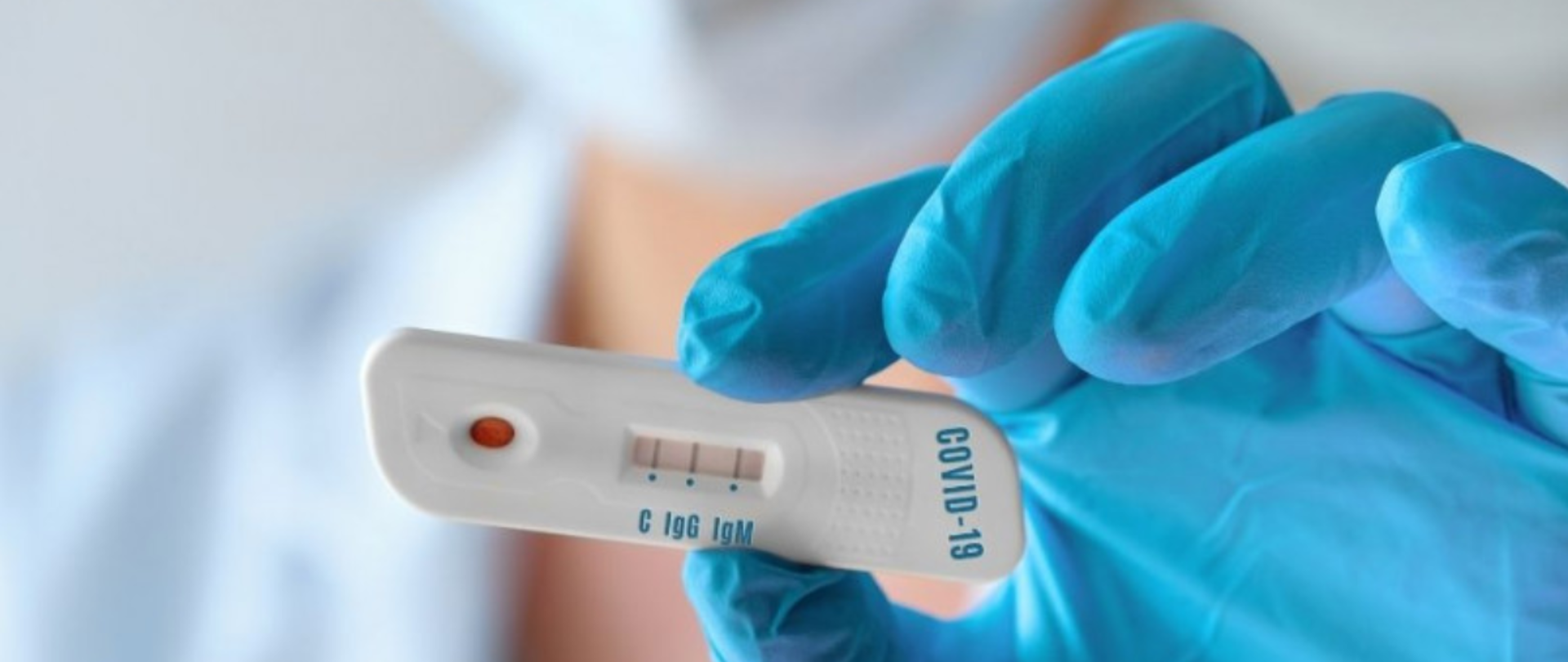 Na zdjęciu ręką w rękawiczce niebieskiej trzymająca test z napisem COVID-19