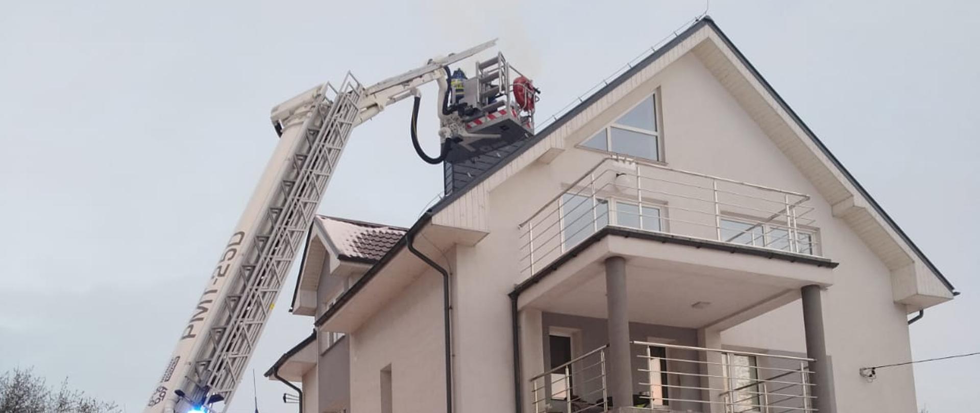 Zdjęcie przedstawia strażaków prowadzących działania ratowniczo-gaśnicze podczas pożaru sadzy w kominie