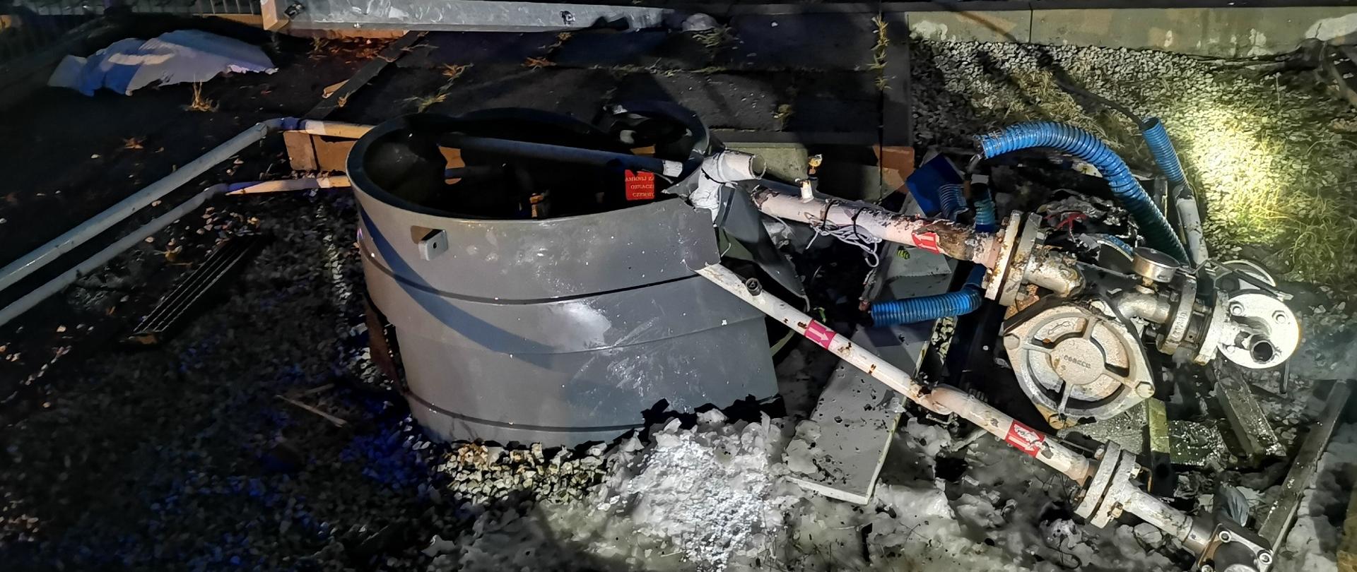 Zdjęcie przedstawia osprzęt napełniania podziemnego zbiornika LPG na stacji paliw, który został uszkodzony przez znajdujący się w tle samochód ciężarowy