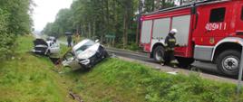 Na zdjęciu po prawej stronie widać na drodze samochód pożarniczy, po lewej stronie na poboczu drogi w rowie widać dwa uszkodzone pojazdy osobowe koloru szarego.