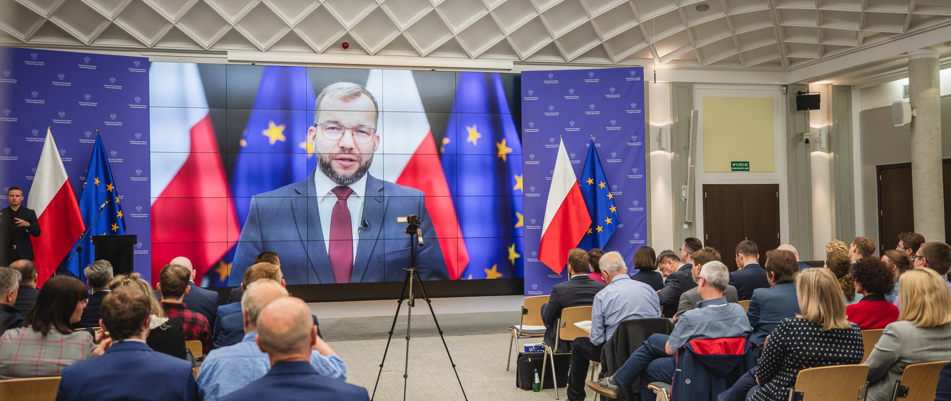 Na ekranie minister Grzegorz Puda przemawia podczas konferencji