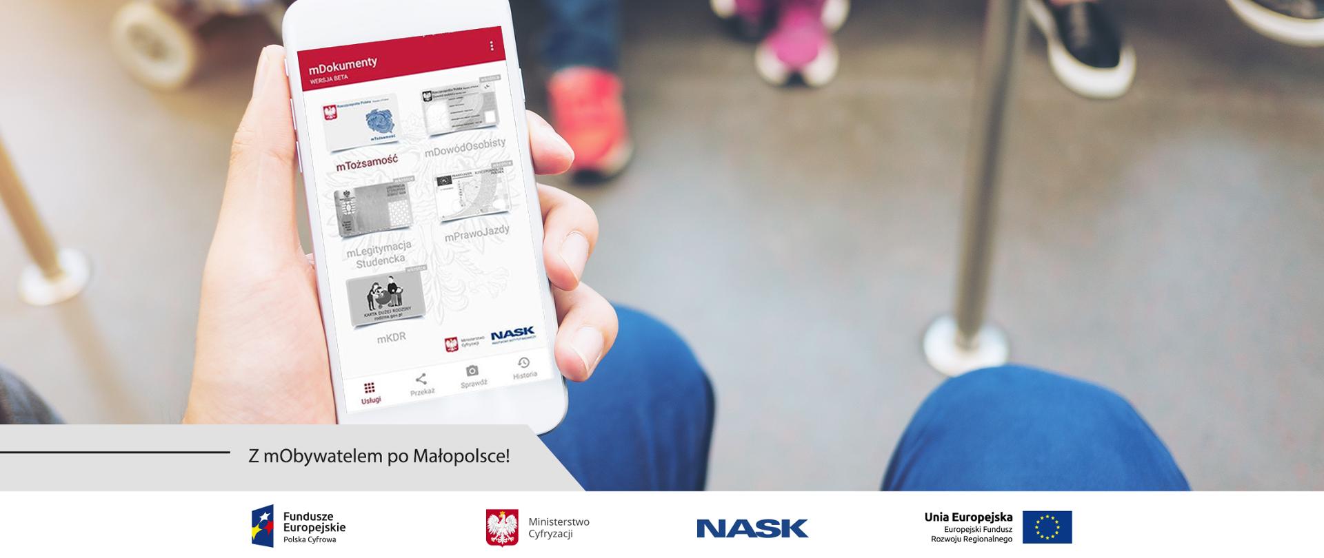 Mężczyzna trzymający w dłoniach smartfon z włączoną aplikacją mObywatel. Obok napis: Z mObywalem po Małopolsce