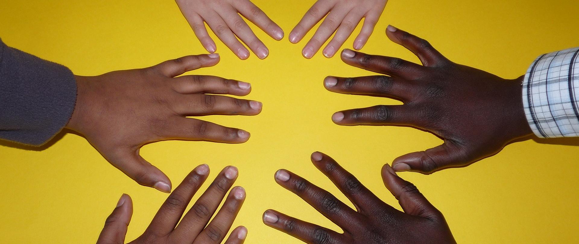 Trzy pary dłoni. Oparte na blacie, zwrócone do siebie.