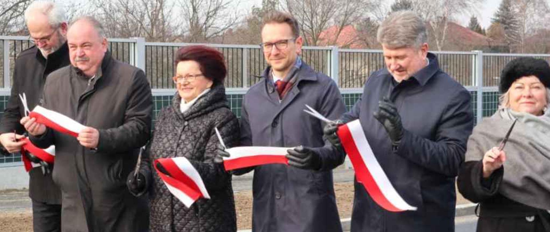Na zdjęciu stoi sześć osób, trzeci z prawej wiceminister Waldemar Buda. W ręku trzymają nożyczki i fragmenty przeciętej biało-czerwonej wstęgi.