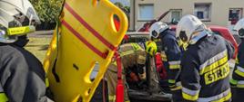 Strażacy ratownicy OSP podczas egzaminu praktycznego szkolenia z zakresy ratownictwa technicznego wykonują dostęp do osoby znajdującej się w pojeździe przy użyciu narzędzi hydraulicznych.