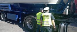 Inspektor kujawsko-pomorskiej Inspekcji Transportu Drogowego wraz z inspektorem Transportowego Dozoru Technicznego kontrolują ciągnik siodłowy z podpiętą naczepą-silosem do przewozu ładunków sypkich.