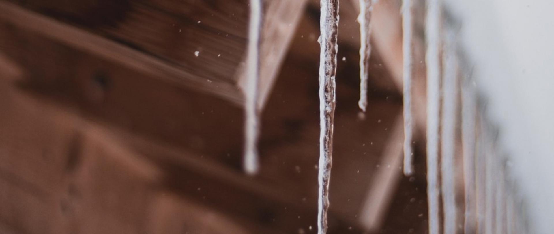 Sople lodu zwisające z drewnianej krawędzi dachu na rozmytym tle.