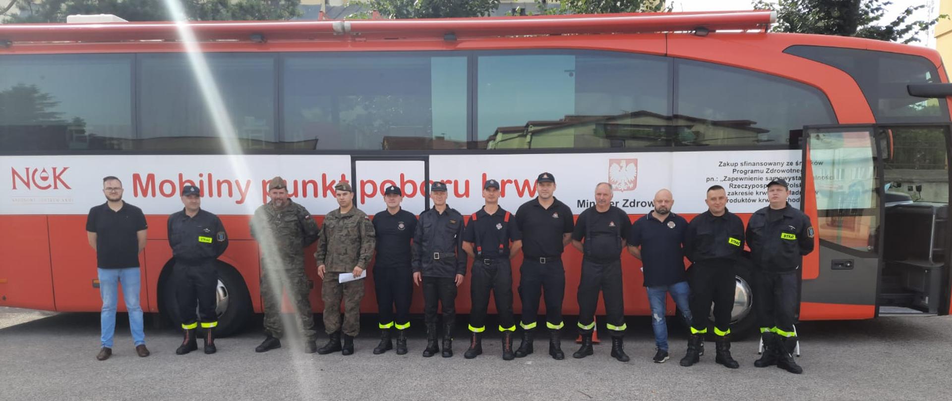 Strażacy PSP i OSP oraz żołnierze WOT na tle krwiobusa. Wszyscy ubrani w mundury.