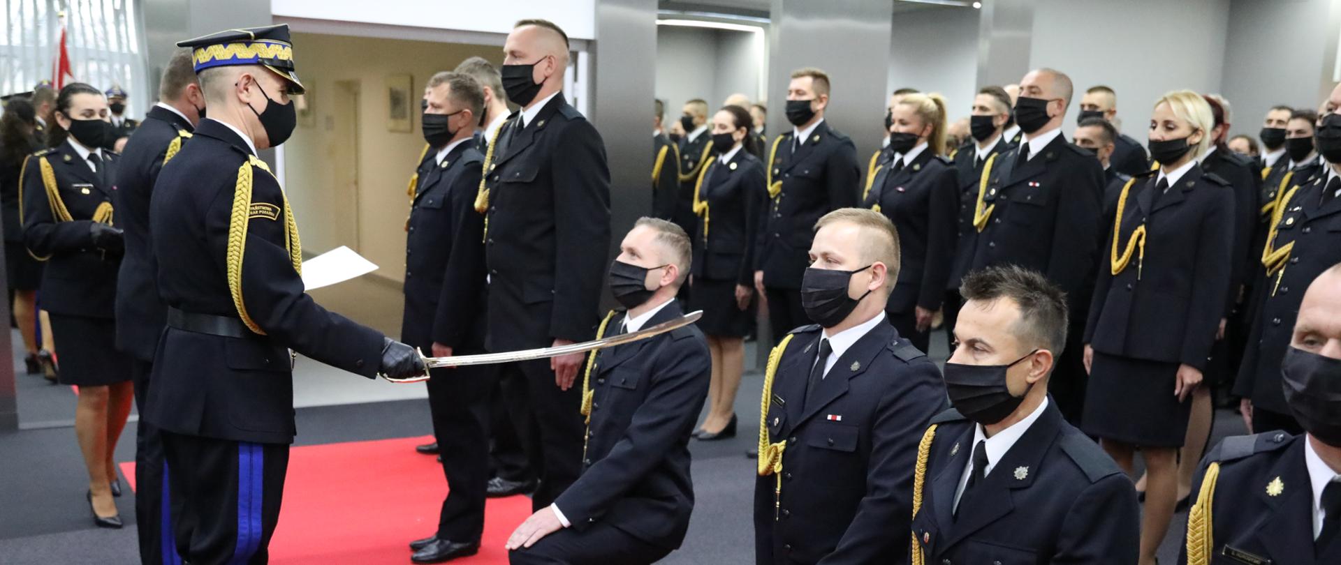 Komendant Główny PSP nadbrygadier Andrzej Bartkowiak i Zastępca Komendanta Głównego nadbrygadier Adam Konieczny w trakcie pasowania na oficera i wręczania aktu nadania pierwszego stopienia oficerskiego funkcjonariuszom PSP. W tle awansowani funkcjonariusze.