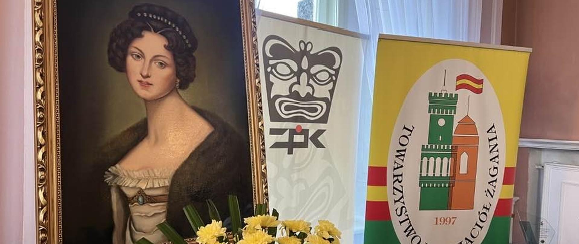 Na zdjęciu od lewej obraz Doroty de Talleyrand-Périgord , baner ŻPK oraz baner Towarzystwa Przyjaciół Żagania. Na dole bkiet żółtych kwiatów.
