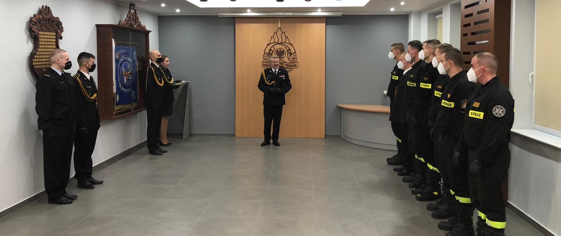 Uroczysta zbiórka z okazji święta niepodległosci na świetlicy KM PSP Sopot. Po prawej w szeregu stoi zmiana słuzbowa w ubraniach koszarowych, po lewej funcjonariusze systemu codziennego w mundurach galowych. po srodku stoi Komendant Miejski PSP w Sopocie i wyglasza przemówienie